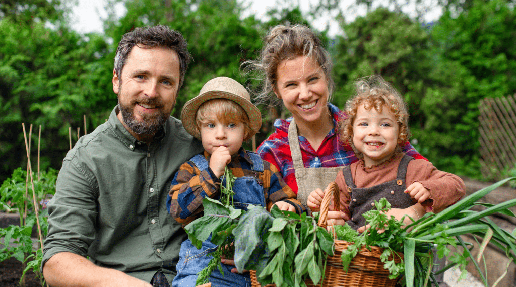 Family gardening together holding basket of fresh vegetables.