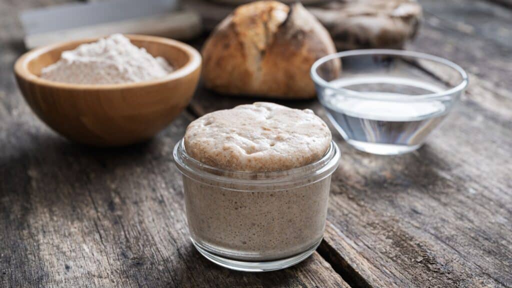 Sourdough starter with flour and water on wooden table.