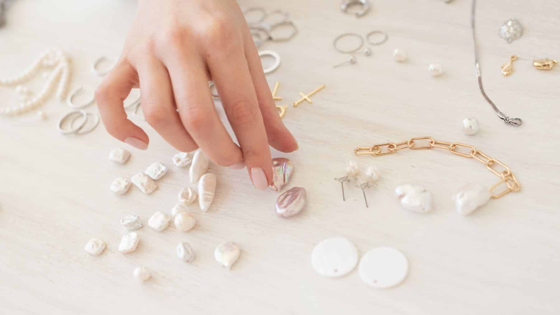 Hand arranging various pearls and jewelry on table.