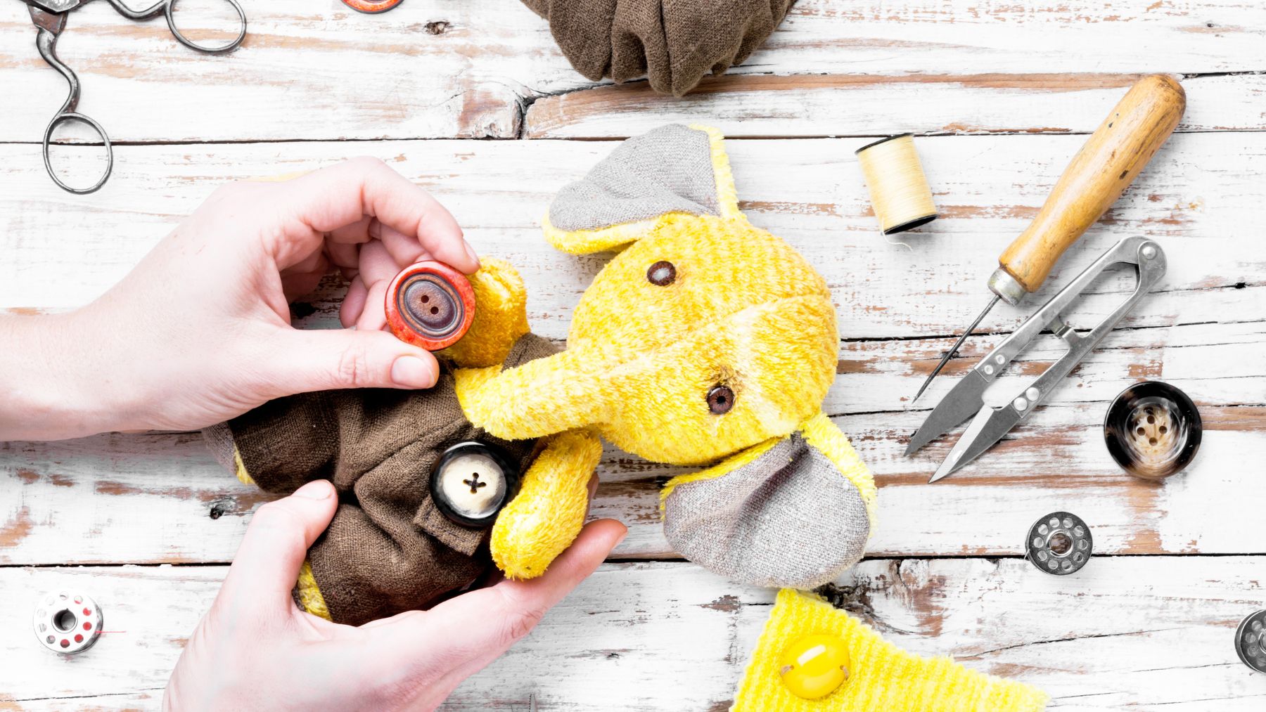 Sewing buttons on stuffed elephant toy with tools.